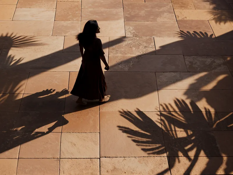 Sombra de una mujer caminando sobre un suelo de baldosas de barro bajo el sol
